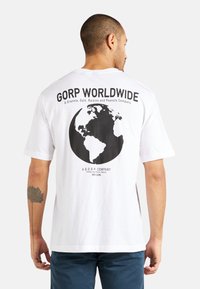 Weißes Baumwoll-T-Shirt mit einem schwarzen Globus-Motiv und dem Text "GORP WORLDWIDE" auf dem Rücken, kurzen Ärmeln und einem lockeren Schnitt.