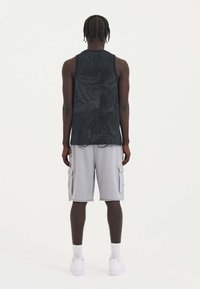 Black tank top with a detailed graphic, paired with light gray cargo shorts featuring side pockets. Footwear is white sneakers.