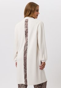 Lange crèmekleurige tuniek met een centraal luipaardprintpaneel. Heeft puffed mouwen en een rechte snit, gemaakt van een zachte stof.