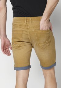 Žuti traper kratke hlače s preklopom, stražnjim džepovima i prilagođenim dizajnom, koje ističu glatku teksturu i strukturiranu siluetu.