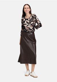 Top à motifs floraux en beige et noir, associé à une jupe en cuir marron foncé et des baskets blanches, présentant une silhouette décontractée.