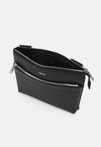 Pochette en cuir noir avec deux compartiments zippés, présentant une texture lisse et un logo embossé, mettant en avant un design minimaliste.