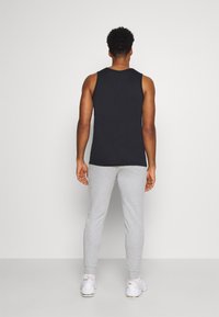 Camiseta sin mangas negra combinada con pantalones de chándal grises, con un ajuste casual y tejido suave, con puños acanalados y zapatillas blancas.