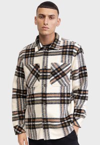 Chemise en polaire à carreaux en ivoire, avec des motifs à carreaux noirs, orange et gris, dotée de deux poches poitrine et d'une fermeture à boutons sur le devant.