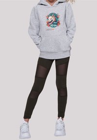 Sudadera gris con un gráfico de dragón, combinada con leggins negros que tienen paneles de malla. Zapatillas deportivas blancas completan el atuendo.