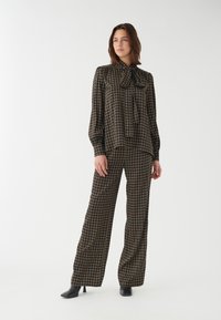 Schwarze und goldene gemusterte Bluse mit einer Schleife und weitem Hosenbein, ausgestattet mit einem geometrischen Design und glattem Stoff.