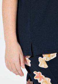 T-shirt blu navy con fessure laterali, realizzata in materiale morbido, abbinata a pantaloni con motivo floreale in rosa chiaro e arancione.