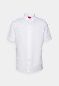 Camisa blanca de manga corta y cuello, confeccionada con un tejido suave. Presenta una etiqueta de marca visible en rojo en la costura lateral.