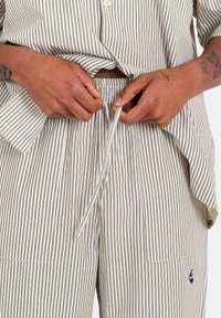 Ensemble de détente en coton rayé comprenant une chemise à boutons avec des manches retroussées et un pantalon à taille élastique avec cordon. Couleurs marine et crème.