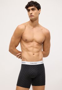 Fekete boxer alsónadrág geometrikus mintával, puha anyagból készült. A derékpánt fehér, "Calvin Klein" márkázással.