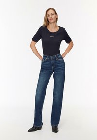 Haut bleu marine à manches courtes avec col rond, associé à un jean droit taille haute bleu foncé. Bottines à talons noires.