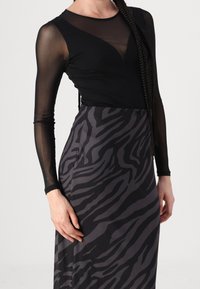 Haut noir à manches longues en tissu transparent, associé à une jupe à motif zèbre gris, avec une silhouette ajustée et un détail subtil au niveau du décolleté.
