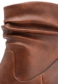 Botte en cuir marron avec une surface douce et texturée, dotée d'un design décontracté. Plis distinctifs et finition naturelle.
