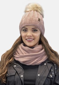 Lyserød strikket hue med en faux fur pom-pom på toppen, parret med et matchende lyserødt strikket tørklæde med tekstureret ribb.