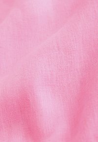 Primer plano de una tela tejida suave de color rosa claro con una textura ligeramente arrugada y un patrón visible de fibras.