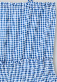 Tissu à carreaux bleu et blanc avec une taille élastique froncée et un bord volanté. Légère, motif texturé avec des bretelles ajustables.