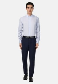 Lichtblauw gestreept overhemdd met navy broeken en een zwarte riem. Glad stof, maatwerk pasvorm en lange mouwen. Zwarte nette schoenen.