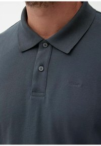 Donkergrijs poloshirt van een gestructureerde stof, met een klassieke kraag, een knoopsluiting met twee knopen en een subtiele geborduurde logo op de borst.