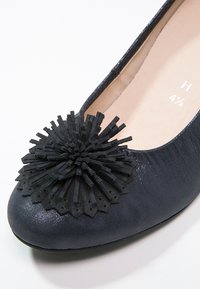 Chaussure plate bleu marine avec un grand pompon texturé noir sur le bout et une doublure intérieure beige marquée taille 4½ H.