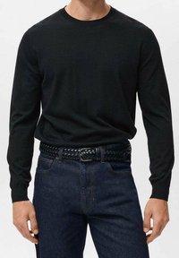 Pull noir à manches longues avec col rond, fabriqué en matière douce, associé à un jean en denim bleu foncé et une ceinture tressée en cuir noir.
