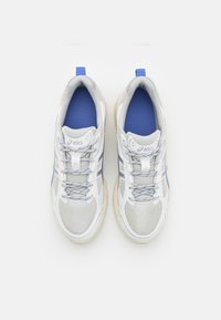 Baskets de sport blanches et grises avec une tige en mesh, des accents bleus et des lacets gris clair. Elles présentent une semelle texturée et une languette arrière.