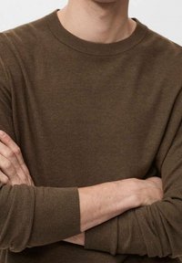 Pull-over en maille marron avec un col rond et des poignets côtelés, présentant un tissu texturé et une coupe décontractée.