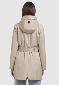 Beige waterdichte jas met een koordkap, een ceintuur in de taille en knoopdetails. Soepele textuur en een getailleerde pasvorm.