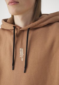 Sudadera marrón con cordones, que presenta un logo en blanco de "7 DAYS ACTIVE". Textura suave, con dos terminales metálicos negros en los cordones.