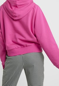 Růžová zkrácená mikina s kapucí a žebrovaným lemem, kombinovaná s kalhotami s vzorem houndstooth v černobílé barvě. Měkká tkanina a volný střih.