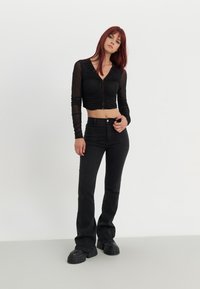 Svart kortermet langermet topp med samlet detalj og knappelukking foran, paret med høytlivede svarte jeans og klumpete svarte plattformsko.