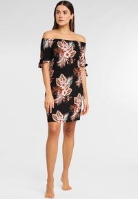 Vestido negro sin mangas con estampado floral en tonos de rosa y beige, con mangas enrolladas y silueta ajustada.