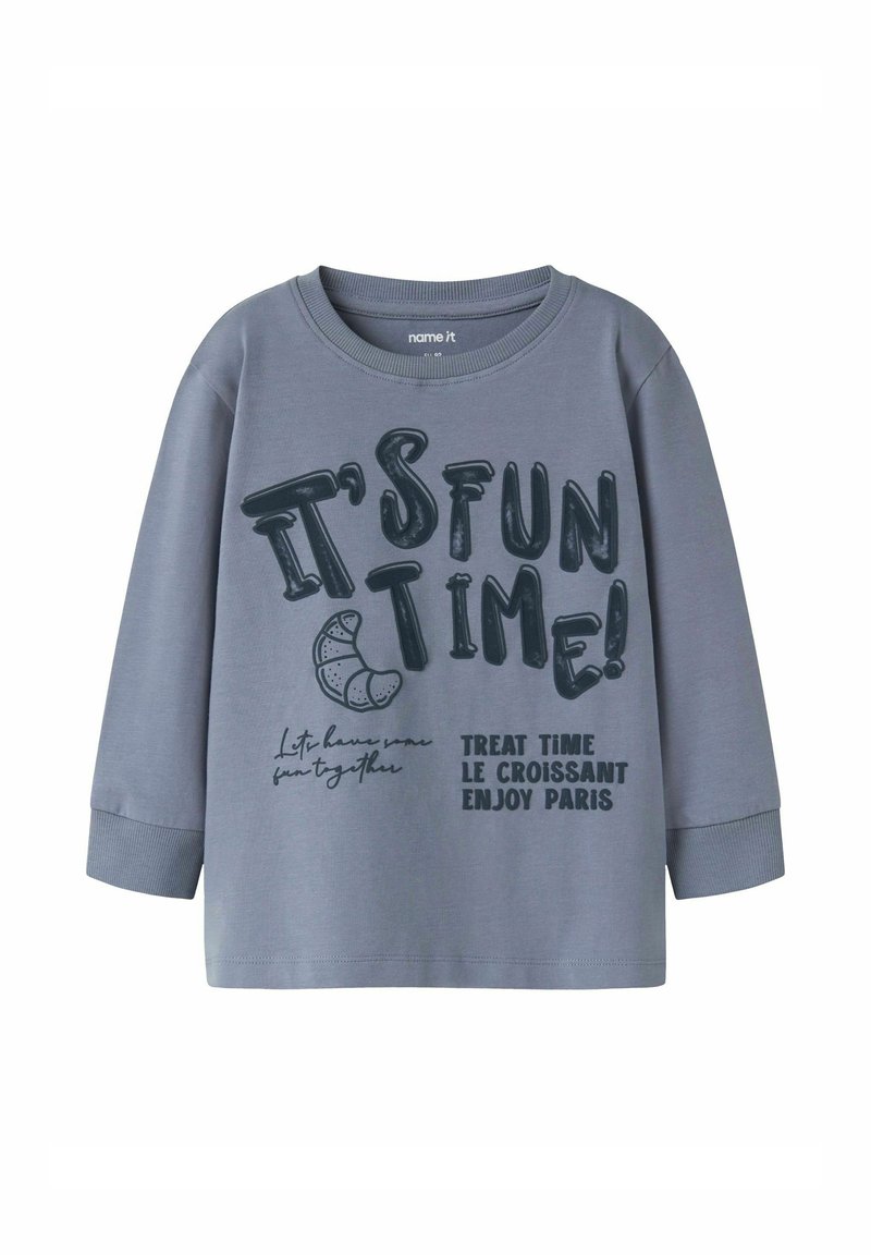 Grijze long sleeve t-shirt van katoen met een ronde hals. Kenmerkt zich door grote zwarte tekst: "HET IS PLEZIER TIJD!" en "BEHANDELING TIJD LE CROISSANT GENIET PARIJS."