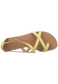 Gul lädersandal med korsande remmar, platt brun sula och minimalistisk design. Har en justerbar vristrem för en säker passform.
