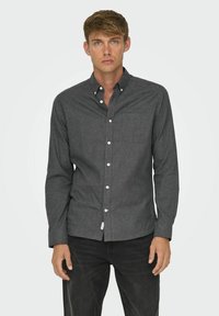 Dark gray button-up shirt made of textured fabric with a single chest pocket, adjustable cuffs, and white buttons. Worn with dark jeans.