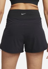 Juodi sportiniai šortai su minkšta, plačia juostele ir lengvu išplatėjimu apačioje. Gale juostos yra mažas pilkas Nike logotipas.
