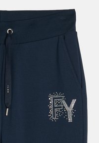Jogging en marine avec une taille côtelée, un cordon de serrage et un détail en strass argenté portant l'inscription "FY" sur la poche gauche. Tissu doux en mélange de coton.