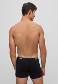 Schwarze Boxershorts mit engem Schnitt, versehen mit einem weißen Logo auf dem Bund. Glattes Material und minimalistisches Design.