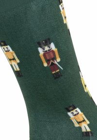 Calzini verdi con un motivo ripetuto di figure di schiaccianoci in vari colori, realizzati in un tessuto morbido con una superficie liscia.