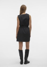 Robe sans manches noire avec des rayures blanches verticales, taille cintrée et coupe droite, assortie à des bottes noires montantes.