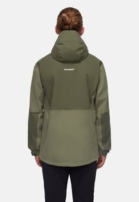 Olivengrøn vandtæt jakke med hætte, der har en høj krave, elastiske ærmer og "MAMMUT" logoet i hvidt på ryggen.