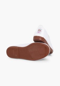 Witte canvas schoenen met een rubberen bruine zool, voorzien van een gestikt ontwerp en een label met een cartoonfiguur op de hiel.