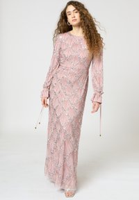 Langes pinkes Kleid mit langen Ärmeln, verziert mit silberner Perlenstickerei in einem diamantenförmigen Muster, hat eine taillierte Taille und einen fließenden Rock.
