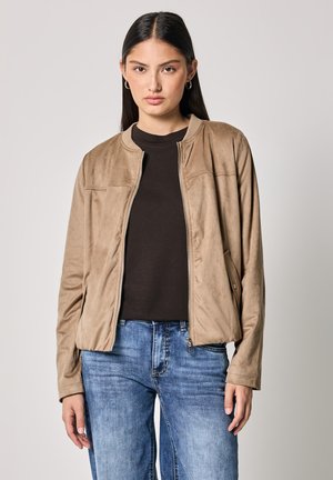 Veste bomber en suède beige avec un col rond, fermeture éclair intégrale et poches latérales, associée à un haut sombre et un jean bleu. Texture lisse.