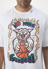 Biely bavlnený tričko s grafikou tigra, ktorý drží basketbal, obklopeného farebnými plameňmi a textom "ŽIADNE ĎALŠIE VÝMLUVY!"