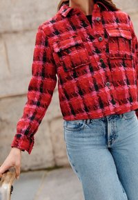 Punainen ja vaaleanpunainen ruudullinen takki, jossa on teksturoitu pinta, kaksi etutaskua, nepparit ja kaulus. Yhdistetty vaaleansinisiin farkkuihin.