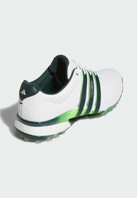 Zapatilla deportiva blanca con un acento verde, tres rayas negras, un talón texturizado y una suela acolchada con una base verde translúcida.