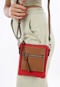 Red and brown crossbody bag featuring a leather front pocket, zipper closure, and an adjustable strap with a metal clasp.
