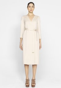 Beżowa sukienka typu wrap z rękawami 3/4; posiada pasek do przewiązania na talii oraz długość do kolan. Gładka tekstura materiału.