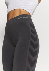 Leggings gris avec une taille haute, présentant un motif en chevron texturé sur le côté et un logo sur la ceinture.