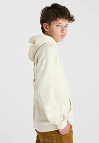 Crème-kleurige hoodie met een kangoeroezak, een verstelbare trekkoordcapuchon en geborduurde accenten in rood en blauw op de mouw.